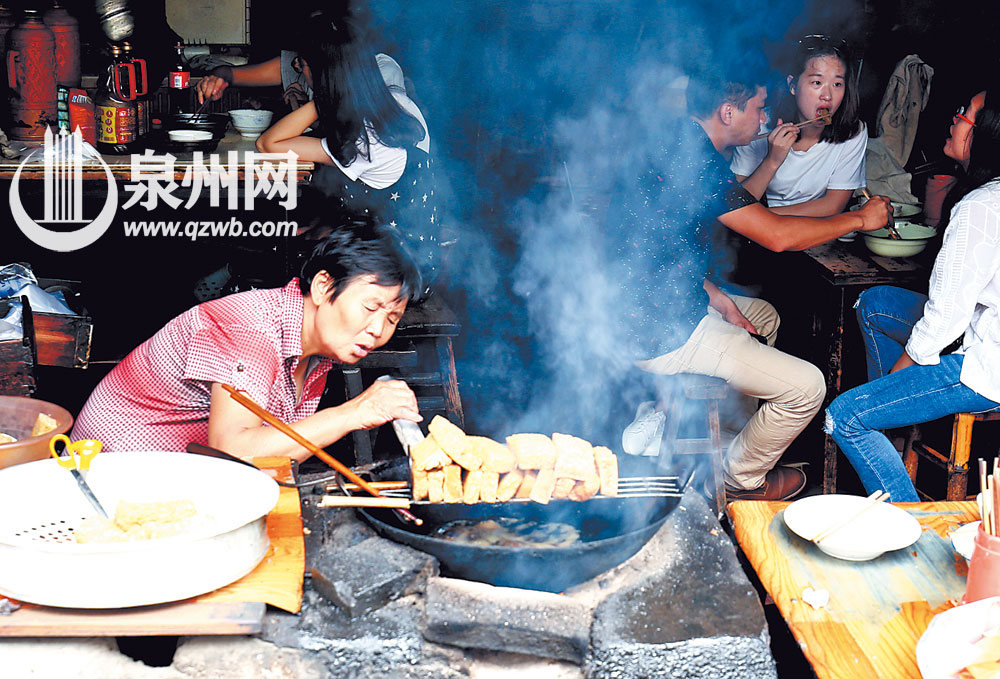 吴秀华阿婆用吹火筒把柴火吹旺，炸粿的火候全凭经验控制。