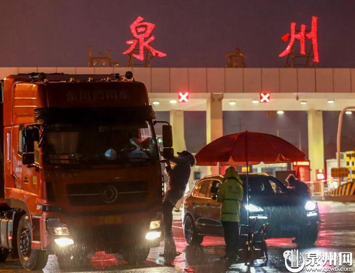 2月15日20时10分，在福厦高速公路泉州收费处，一名志愿者攀在货车上，给雨中的大货车司机测量体温。（陈英杰 摄）