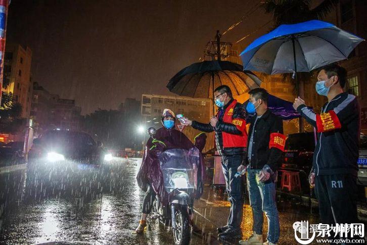 2月15日23时25分，在泉州市区丰泽东凤社区，社区志愿者正在冒雨给出入社区的人员测量体温。（陈英杰 摄）