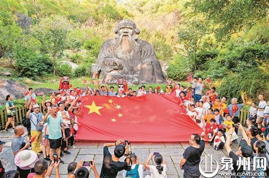 国庆假日期间，泉州市部分景点推出“我与国旗同框”的“打卡”活动。图为10月2日，在泉州清源山老君岩前，市民和游客在一面巨大的五星红旗前合影留念。 （陈英杰 摄）